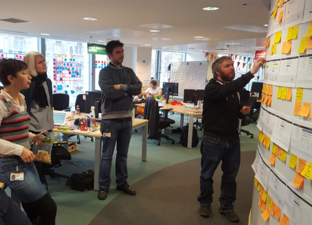 Photo of GOV.UK Notify team at a playback session in front of an agile wall with post-its on
