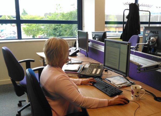 Photo of a webchat advisor looking at a desktop computer screen wearing a headset and using a mouse 