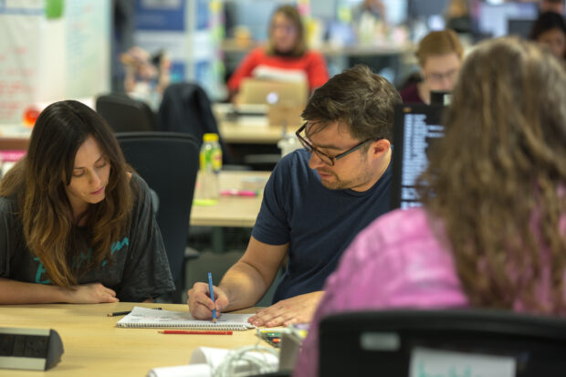 Two colleagues sit at a table and both look at a document where they're drawing their ideas 